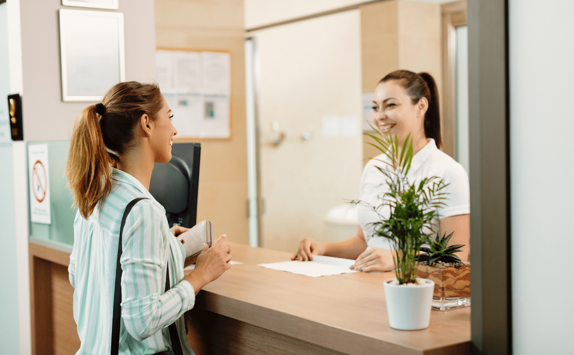 Recepcionista sonriente atendiendo a una clienta en un mostrador, representando una buena experiencia del cliente (CX) y servicio al cliente de calidad.